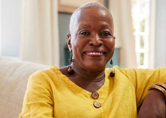 Image of a middle-aged African-American woman sitting on a couch and smiling at the camera