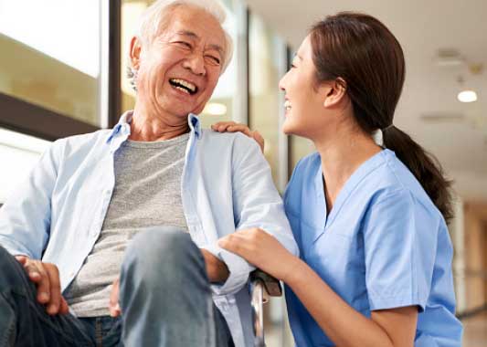 Image of a young asian caretaker laughing with an asian senior man in a wheelchair