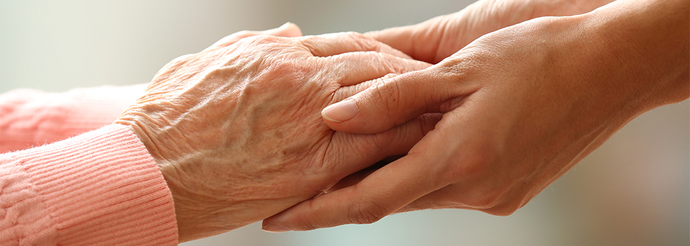 Image of an elderly woman and young woman holding hands